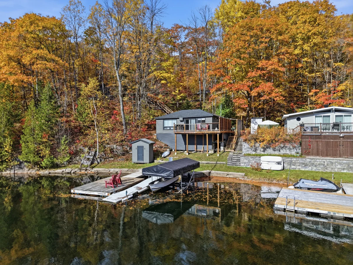 Vue en hauteur d’un chalet au bord de l’eau, des quais et des arbres d’automne reflétés dans l’eau calme