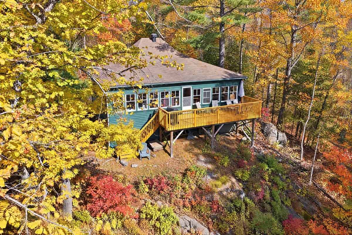 Chalet vert avec un long balcon en bois parmi les arbres dorés et rouges en automne