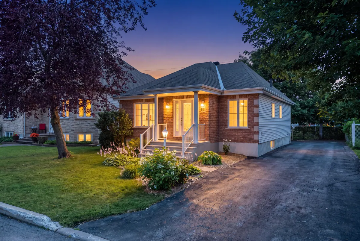 Bungalow en brique au crépuscule avec lumières chaudes brillant aux fenêtres