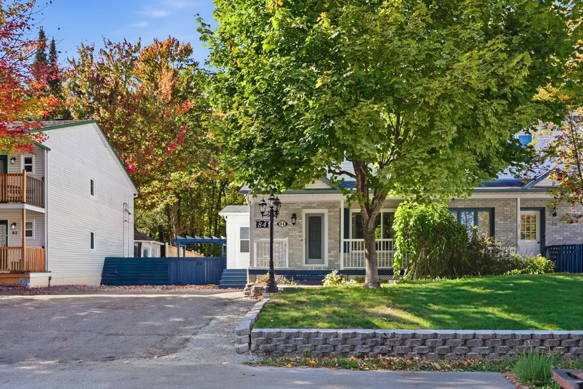 Maison à façade de pierre avec porche couvert, grand arbre et pelouse aménagée