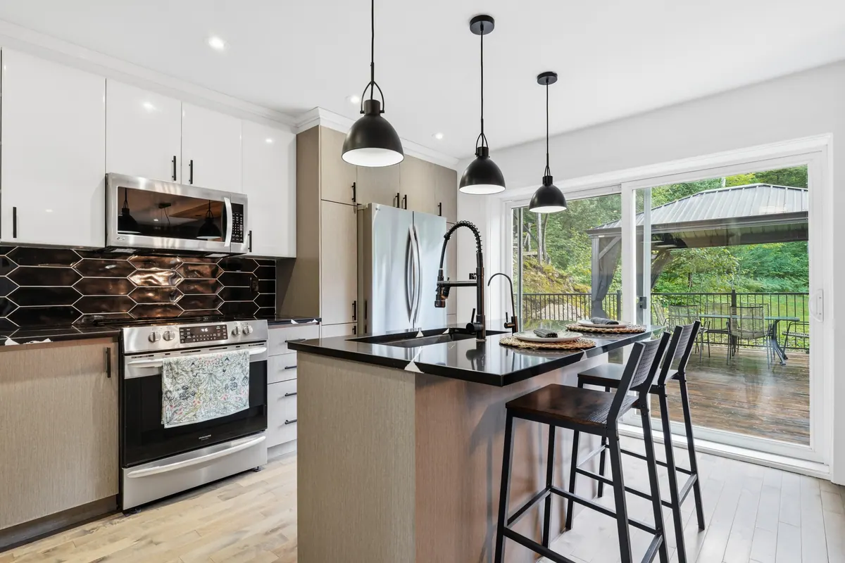 White kitchen with black pendant lights, an island and a view to a covered deck